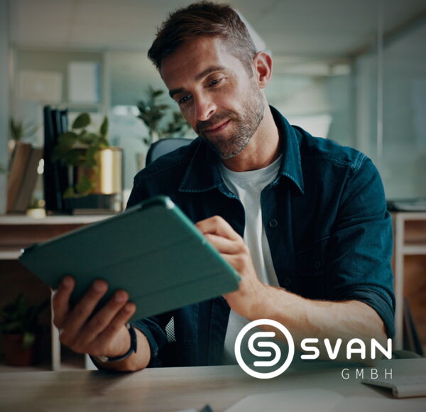 Zufriedener Mann im blauen Hemd am Tablet, der gerade eine Eingabe macht. Er sitzt am Schreibtisch , man sieht ihn von vorne und somit das grüne Tablet von hinten.